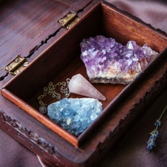 Witch tools inside beautiful old wood box. Rose quartz pendulum, natural amethyst and celestite crystal clusters. Dry lavender flowers on dark purple cloth. Alternative lifestyle concept. Witch tools inside beautiful old wood box. Rose quartz pendulum, natural amethyst and celestite crystal clusters. Dry lavender flowers on dark purple cloth. Alternative lifestyle concept.