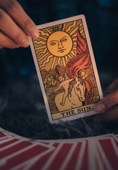 Fortune teller holding THE SUN card and tarot cards. tarot cards and burning candles. Astrologists and forecasting concept.
